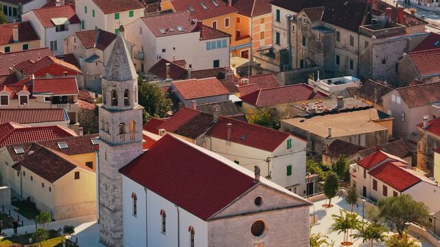 Aerial drone view St. Anastasia's Church, focusing on its Romanesque stone bell tower surrounded by typical Dalmatian residential architecture. Biograd na Moru, Croatia