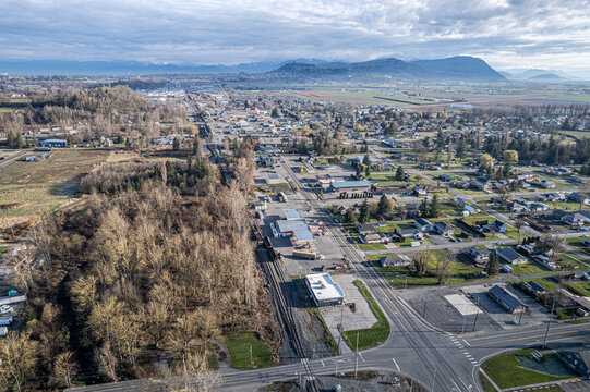 Aerial view of a tranquil town nestled amid golden fields and evergreen forests, with mountains painting the horizon in hazy blues, Sumas, Washington, United States.