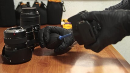 Close-up of photographer cleaning camera with air blower. Camera maintenance, dust removal, photography equipment care, technology and precision concept.