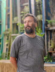 A man with a beard and a gray shirt is standing in front of a building. He looks serious and is looking up at something