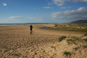 Woman standing on empty sandy beach overlooking ocean