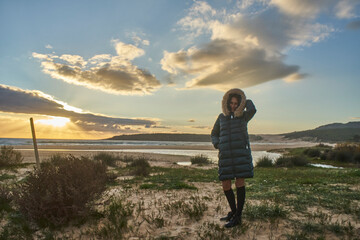 Woman wearing winter coat enjoying cold beach sunset