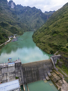 Aerial view of a concrete dam holding back emerald waters amid steep, verdant mountains, a tranquil power amidst the rugged landscape, Long Phu, Soc Trang, Vietnam.