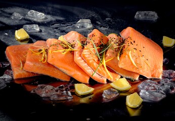 Delicate slices of fresh Salmon are presented with lemon zest and scattered lemon wedges, nestled amongst glistening ice cubes on a reflective black surface © Damian