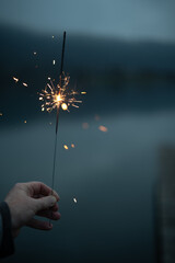 A hand holds burning sparkler in the evening dusk. Vertical background for christmas and new year's with space for text.