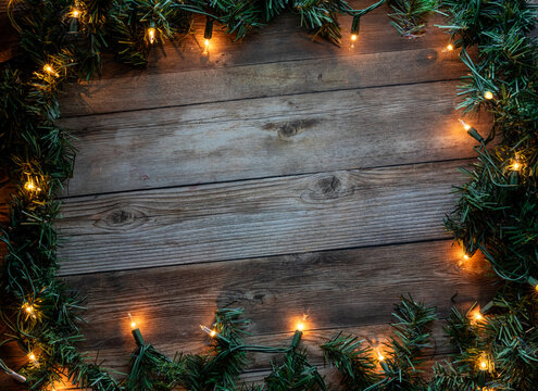 A dark rustic wooden background with pine branches and holiday lights. - Powered by Adobe