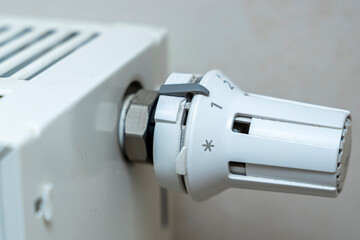 Close-up of a white radiator thermostat control dial set between two temperatures. Useful for demonstrating heating systems, home comfort, and energy efficiency.