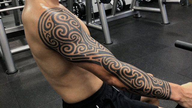 Dense spiral pattern tribal tattoo sleeve on muscular arm in gym