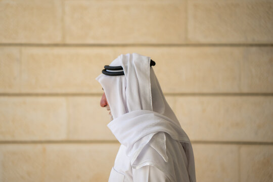 An adult Muslim man in white traditional clothes looks at the camera and expresses emotions. Elderly male sheikh on a background. High quality photo