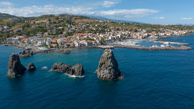 Aerial view of the town of Aci Trezza overlooking the Ionian Sea, in the province of Catania, Sicily, Italy. In the foreground, off the coast, are the Cyclopean Isles. In the background is Mount Etna.