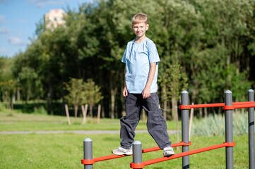 Teen boy standing on parallel bars at outdoor sports ground, fitness exercise and healthy lifestyle training in summer