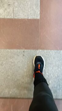 Urban commuter preparing to board train, Foot positioned close to platform boundary on tiled surface, Passenger standing carefully beside yellow safety mark Vertical shot taken on mobile device.