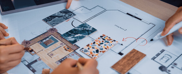 A group of diverse individuals examines a detailed architectural floor plan, highlighting areas for design improvements with thoughtful annotations and a miniature model. SACTR