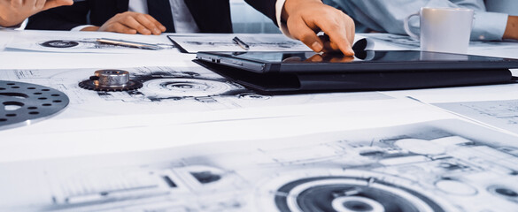 A dynamic scene showcasing business professionals engaged in a collaborative design project. The image highlights a digital tablet and blueprints on a modern office table. SACTR