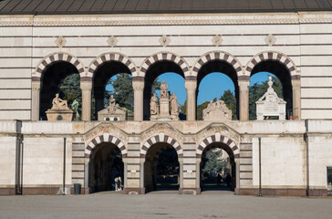 Naklejka premium Striped marble arcade with monumental arches and sculptural tombs at entrance of Monumental Cemetery in Milan, Italy, under clear blue sky.