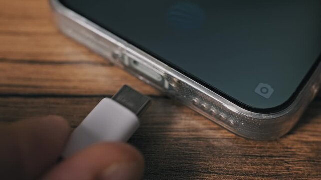 Macro shot of a hand unplugging a white USB-C data cable from a mobile phone in a transparent case. The screen shows a charge percentage notification as the device disconnects.