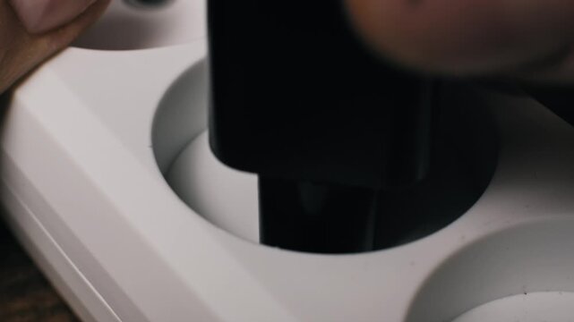 Macro shot of a black European plug with metal prongs inserting into white plastic socket holes. This connects a device to the power supply ensuring a secure electrical connection.