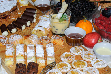 Assorted desserts and pastries on a rustic wooden table with cakes, cookies, chocolate rolls, custard, fresh berries and fruit, perfect for buffet, catering or celebration.