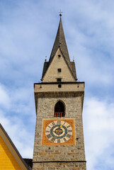 Historic stone clock tower with pointed spire and ornate clock face against a blue sky, showcasing European architecture, heritage and timeless urban landmark.