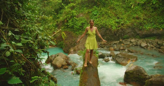 Woman balancing with outstretched arms on log over turquoise river in jungle Costa Rica