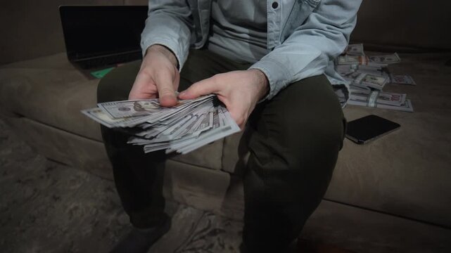 Hands fanning US hundred dollar bills on sofa with laptop nearby. Cash bundles in background. Wealth income hustle concept. Cash Stacks and Laptop for Online Income