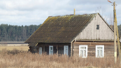Old wooden house in rural area with overgrown vegetation and cloudy sky near forest during daytime © Сергей Семенов