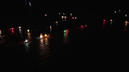 Colorful grave lanterns burning on wet cobblestones at night, candlelight reflections honoring all saints' day and remembering the deceased with solemn, flickering flames