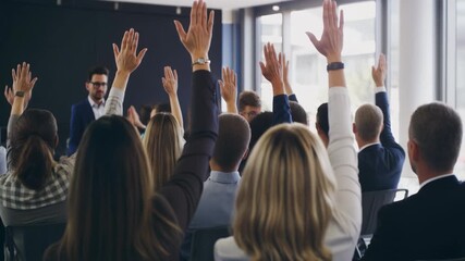 Audience of business people raising their hands to ask questions during a corporate seminar. Male caucasian presenter leading an interactive presentation for professional development