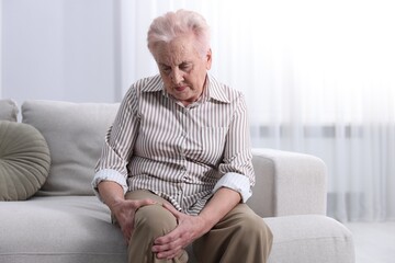 Senior woman suffering from knee pain at home. Rheumatism symptom