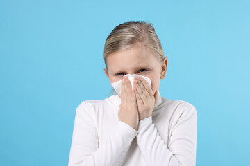 Little girl with runny nose on light blue background. Cold symptom