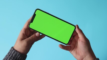 Female hand holding a phone with a green screen horizontally on a light blue background.