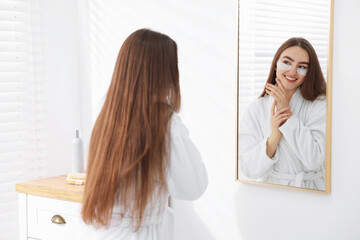 Fototapeta premium Beautiful woman in bathrobe with eye patches near mirror in bathroom