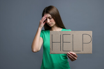 Woman holding cardboard sign with word Help on grey background, selective focus
