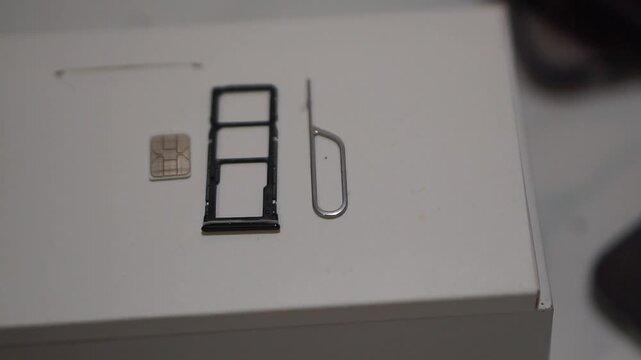 Mobile phone SIM card setup with tray and ejector tool, symbolizing smartphone hardware and cellular connection.