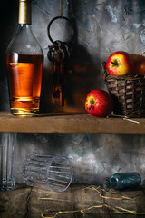 A bottle of cognac and red apples on a wooden shelf