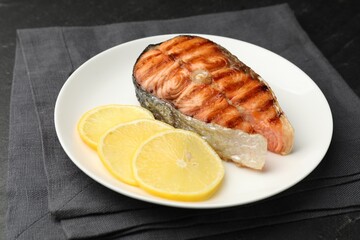 Tasty grilled salmon steak served with lemon on black table, closeup