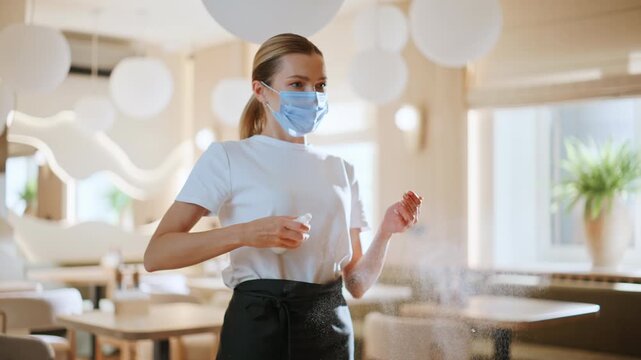 Waitress woman sanitizing hands at light modern restaurant workplace closeup