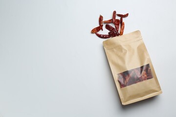 Stand-up pouch with dried chili peppers on light background, top view. Space for text