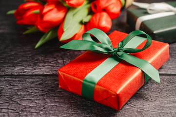 Red gift box with ribbon and fresh red tulip flowers. Easter or birthday holiday black background.