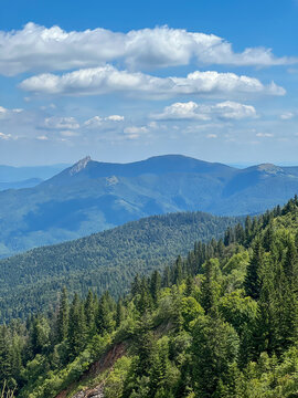 Scenic summer view of Jahorinski Klek ridge near Sarajevo, featuring lush green forests, layered mountain slopes, and a bright blue sky with scattered clouds.