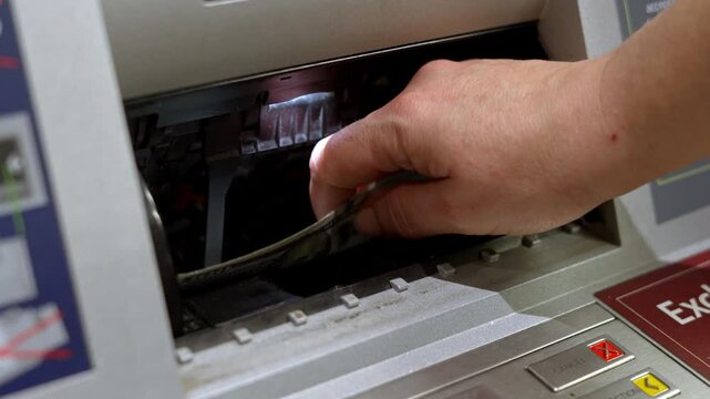 Hand reaching into ATM cash dispenser and taking US hundred dollar bills. Cash withdrawal transaction and banking money access concept