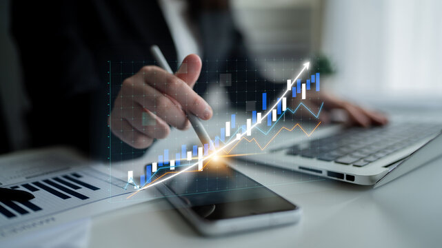A businesswoman analyzes a growth chart displayed on her smartphone while using a laptop, showcasing modern financial analysis and data visualization. Impute - Powered by Adobe