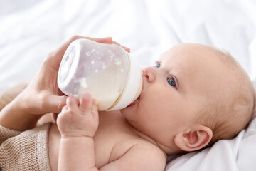 Mother feeding her newborn baby with bottle on bed indoors, closeup