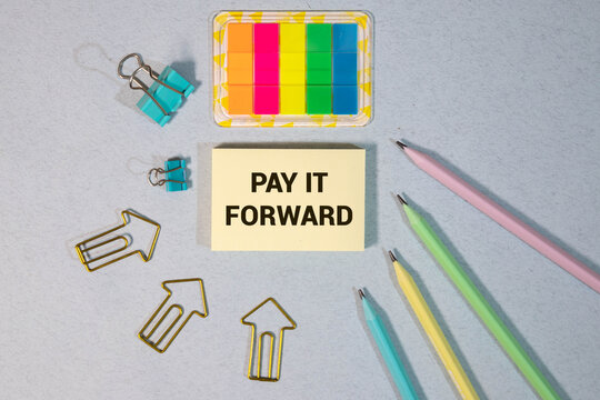 PAY IT FORWARD text on a notebook with pen on wooden background.