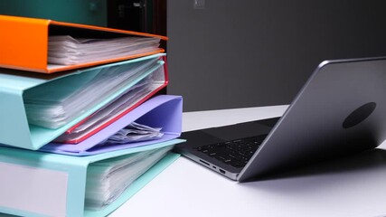 Stack of colorful office binders and a modern laptop on a white desk, representing data management, organization, and administrative tasks in a professional setting - Powered by Adobe