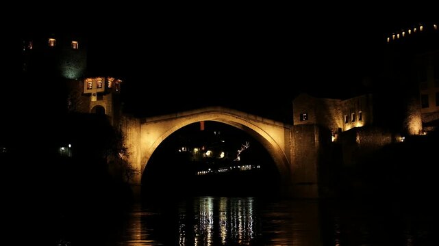 Night view of the historic Stari Most bridge in Mostar, Bosnia and Herzegovina. Illuminated stone arch over the river with reflections, old town architecture and dramatic evening atmosphere.