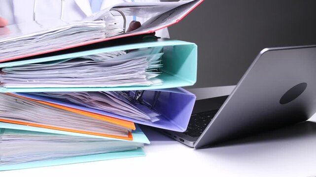 Doctor attending to a large stack of patient files and documents, indicating an overwhelming amount of administrative work and bureaucracy in a medical office setting