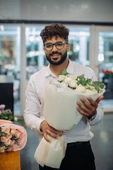 Florist standing in flower shop holding white roses bouquet