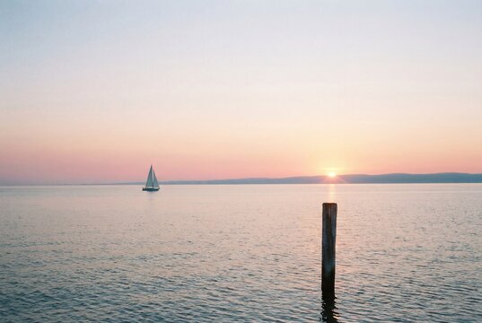 Sailboat on calm sea at sunset with wooden post - Powered by Adobe