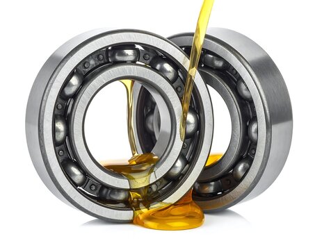 Oil is poured over two metal ball bearings resting on a white background, a mechanical maintenance process